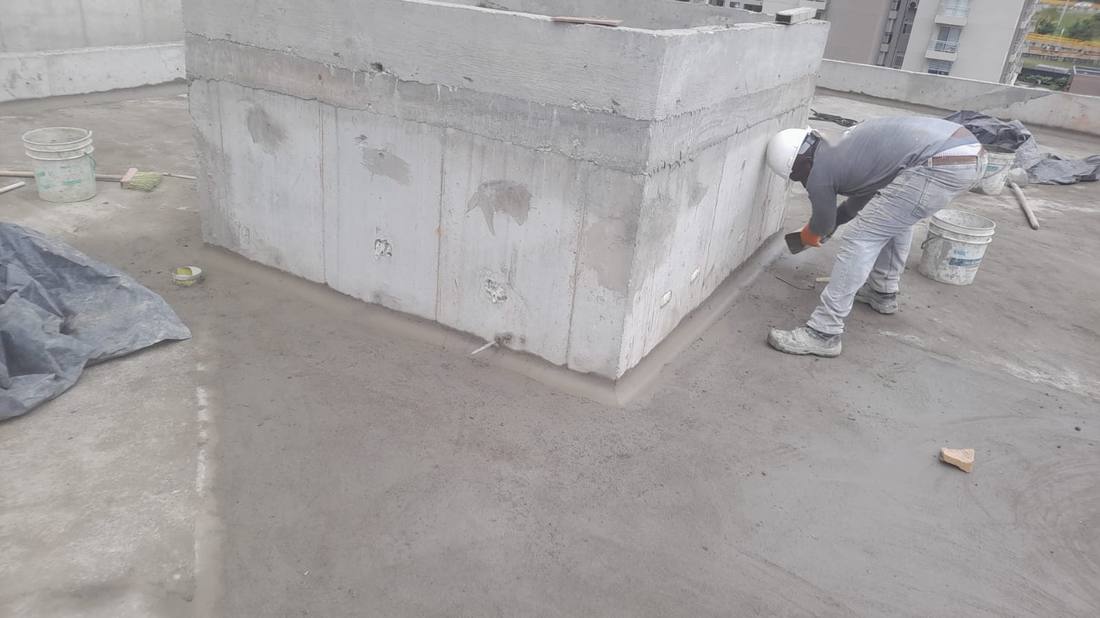 Operario formando una media caña con mortero en la base de un muro de cubierta